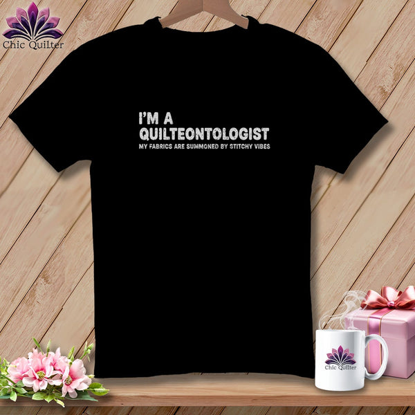 Black t-shirt with white text "I'M A QUILTEONTOLOGIST MY FABRICS ARE SUMMONED BY STITCHY VIBES".