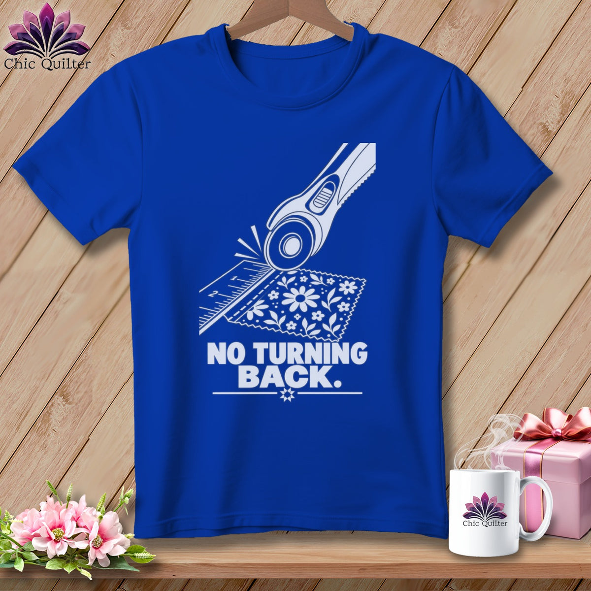 Blue t-shirt with rotary cutter, ruler, and floral fabric graphic and text "NO TURNING BACK."