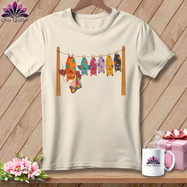 Cream t-shirt with colorful bats hanging on a clothesline with a patchwork quilt.