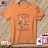 Orange t-shirt featuring three birds wearing glasses, floral wreaths, and holding sewing supplies with text.