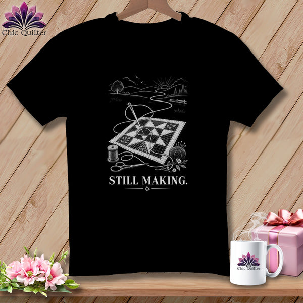 Black t-shirt with quilting motif and "STILL MAKING." text, next to a mug and gift.