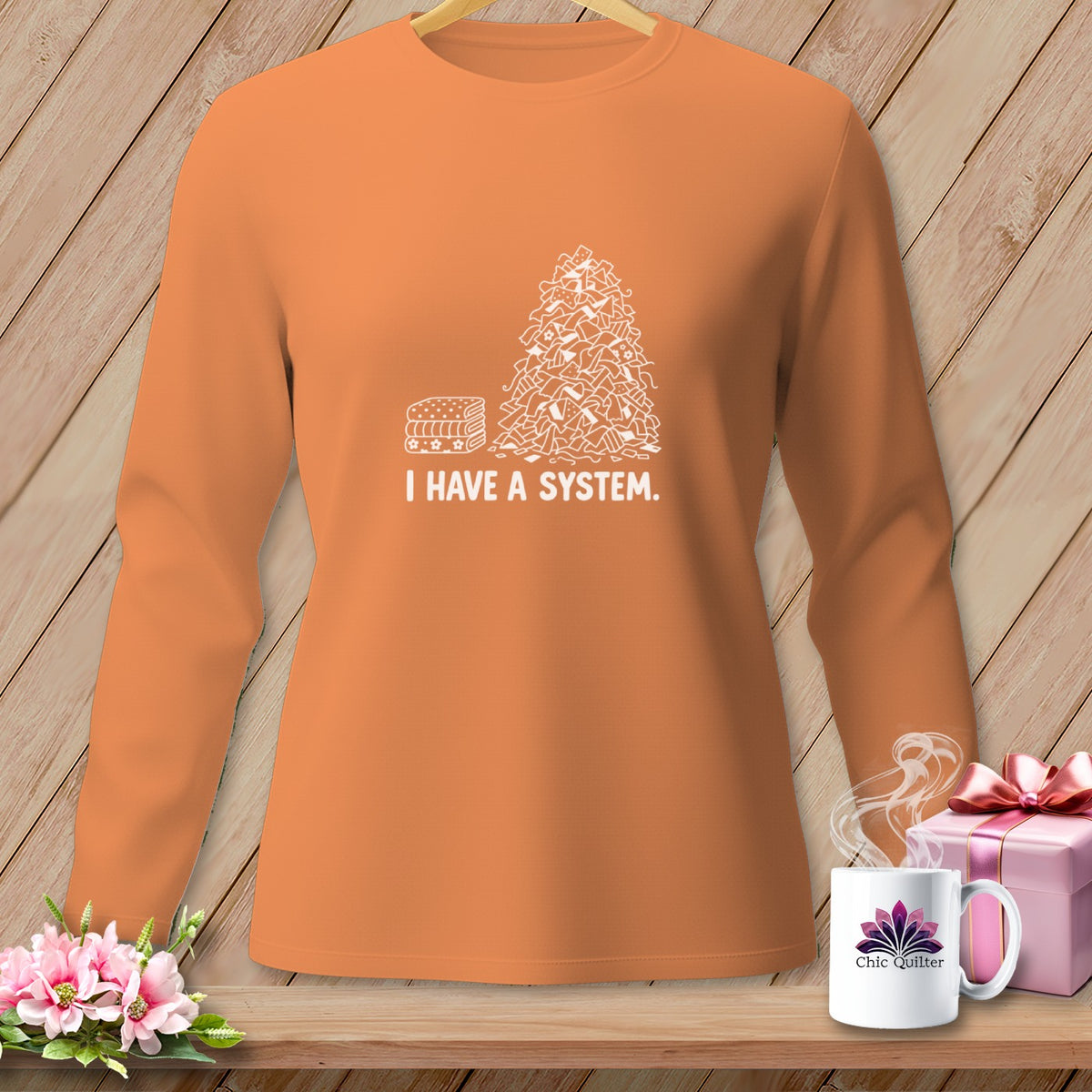 Orange long-sleeve shirt with white graphic of fabric scraps and text "I HAVE A SYSTEM."