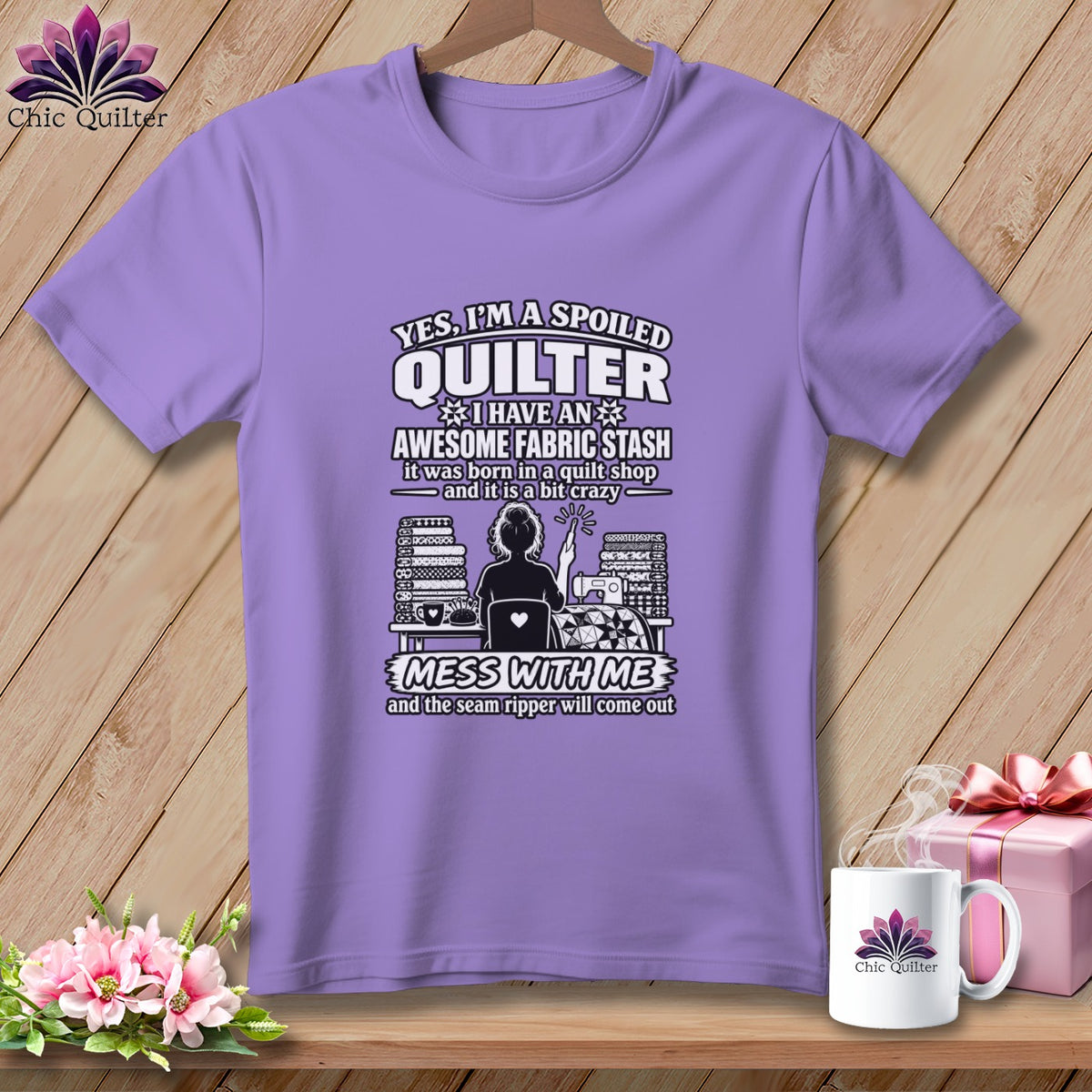 Light purple t-shirt featuring a quilting graphic and funny text, hanging against a wooden background.