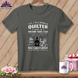Dark gray t-shirt featuring quilting text and a graphic, hanging on a wooden background with accessories.