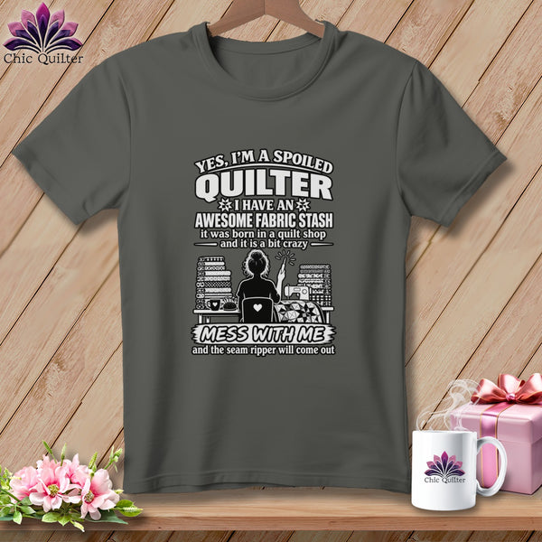 Dark gray t-shirt featuring quilting text and a graphic, hanging on a wooden background with accessories.