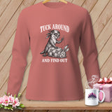 Dusty pink long-sleeve t-shirt with a graphic of an otter sewing a rabbit into a quilt, featuring the text TUCK AROUND AND FIND OUT.
