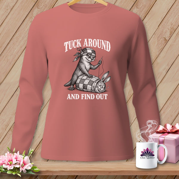 Dusty pink long-sleeve t-shirt with a graphic of an otter sewing a rabbit into a quilt, featuring the text TUCK AROUND AND FIND OUT.