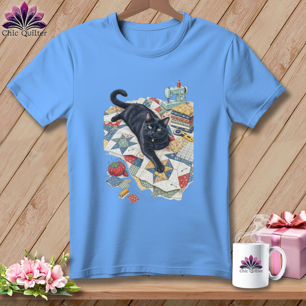 Light blue t-shirt with black cat and quilting supplies illustration.