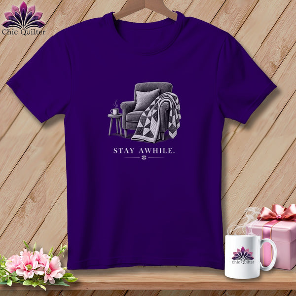 Purple t-shirt with armchair, quilt, and mug graphic; "STAY AWHILE." text.