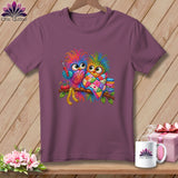 A purple t-shirt featuring a colorful graphic of two whimsical owls perched on a branch with sewing accessories.