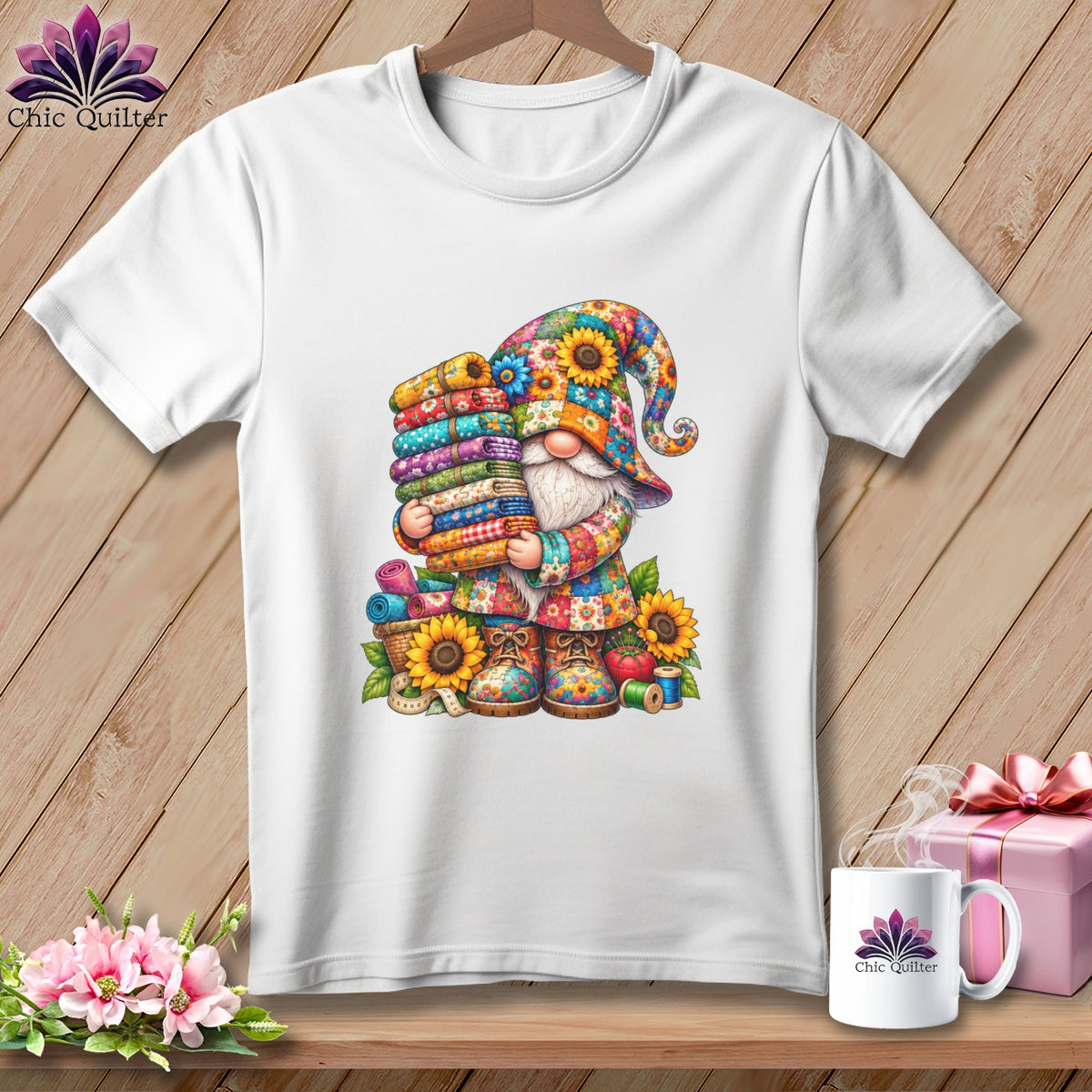 A white crewneck t-shirt featuring a colorful illustration of a gnome holding stacked folded fabrics.