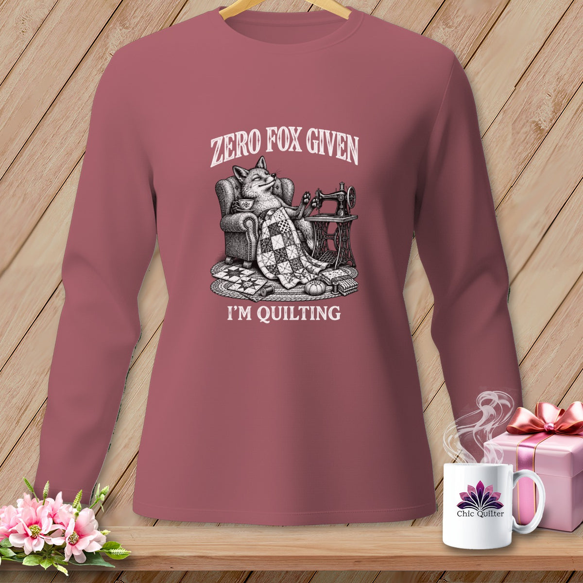 Long-sleeved shirt with a fox sitting in a chair with a quilt and sewing machine. Text reads "Zero Fox Given I'm Quilting."