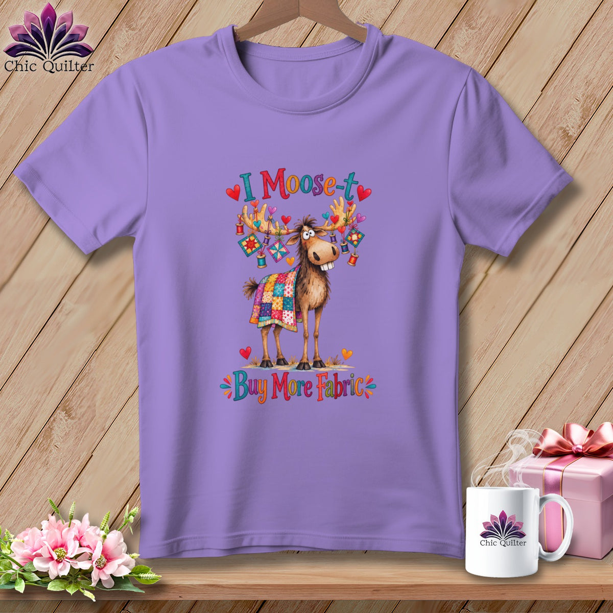 A purple short-sleeved t-shirt featuring a cartoon moose, quilts, hearts, and the text I Moose-t Buy More Fabric.