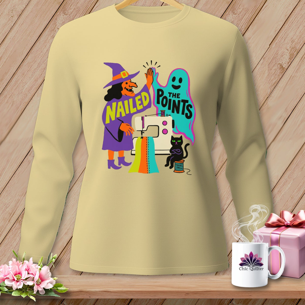 Cream long-sleeve shirt with witch, ghost, sewing machine, and text "Nailed The Points".