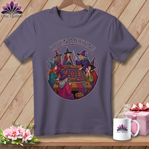 T-shirt with witches gathered around a quilt, text reads "Coven Meeting".