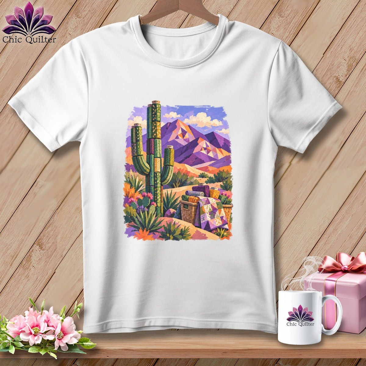 A white t-shirt hanging on a wooden background features a colorful graphic of a desert landscape with purple mountains and a saguaro cactus.