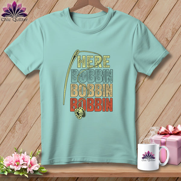 Light blue t-shirt with vintage text "HERE BOBBIN BOBBIN BOBBIN" and sewing needle graphic.