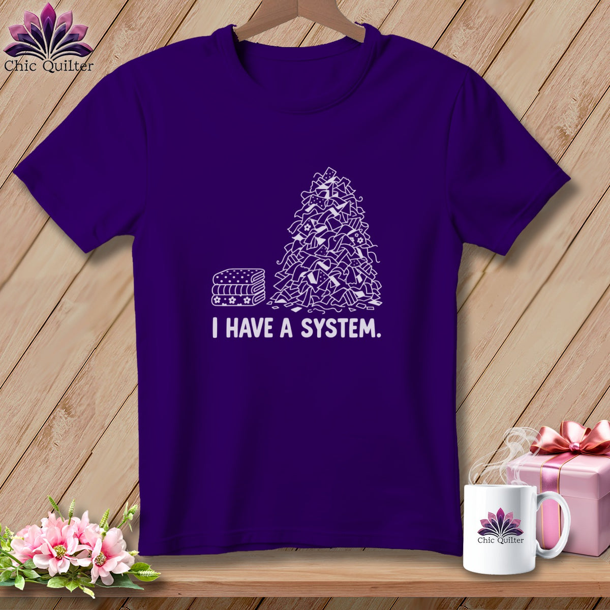 Purple t-shirt with a white graphic of a pile of fabric scraps and a stack of folded fabric.