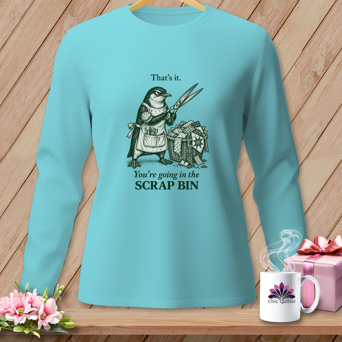 Teal long-sleeve shirt with a penguin holding scissors over a scrap bin.