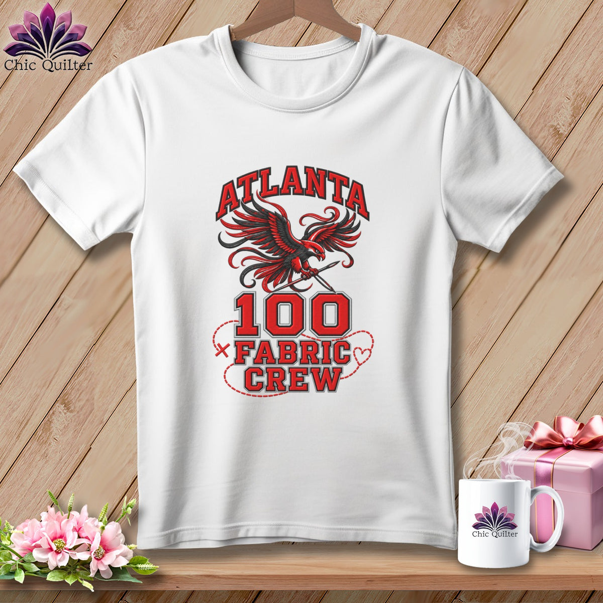 A white t-shirt hanging against a wooden background, featuring a red and black Atlanta Fabric Crew graphic with an eagle.
