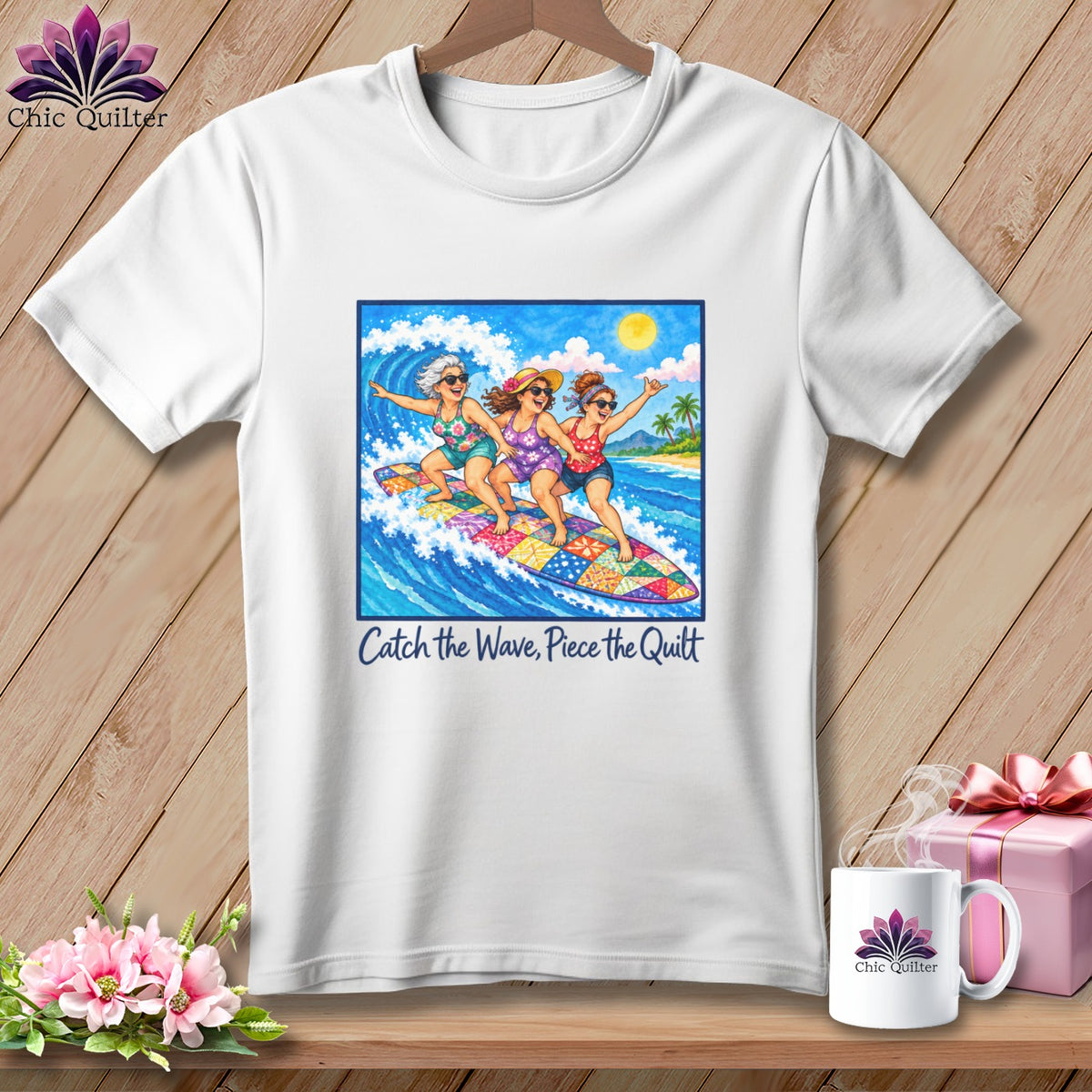 White t-shirt featuring three women surfing on a patchwork surfboard and the text Catch the Wave, Piece the Quilt.