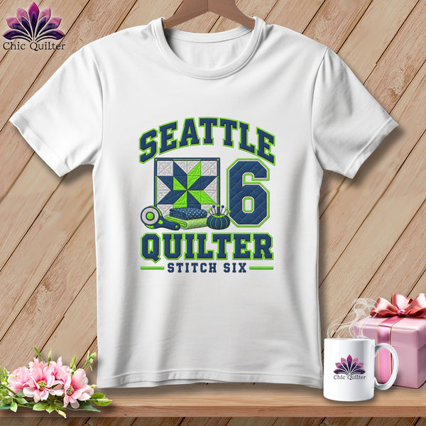 White crewneck t-shirt with blue and green Seattle Quilter graphic on a wooden background.