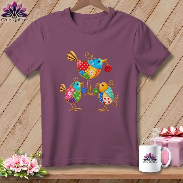 A purple t-shirt featuring a colorful patchwork design of three stylized birds on a wooden background.