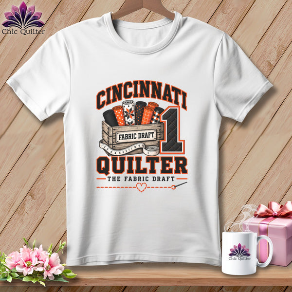 White t-shirt with a graphic of fabric rolls in a crate and text reading Cincinnati Quilter.
