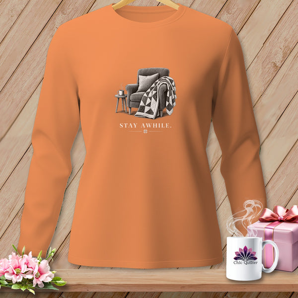 Long sleeve orange shirt with a drawing of an armchair, quilt, and coffee cup.