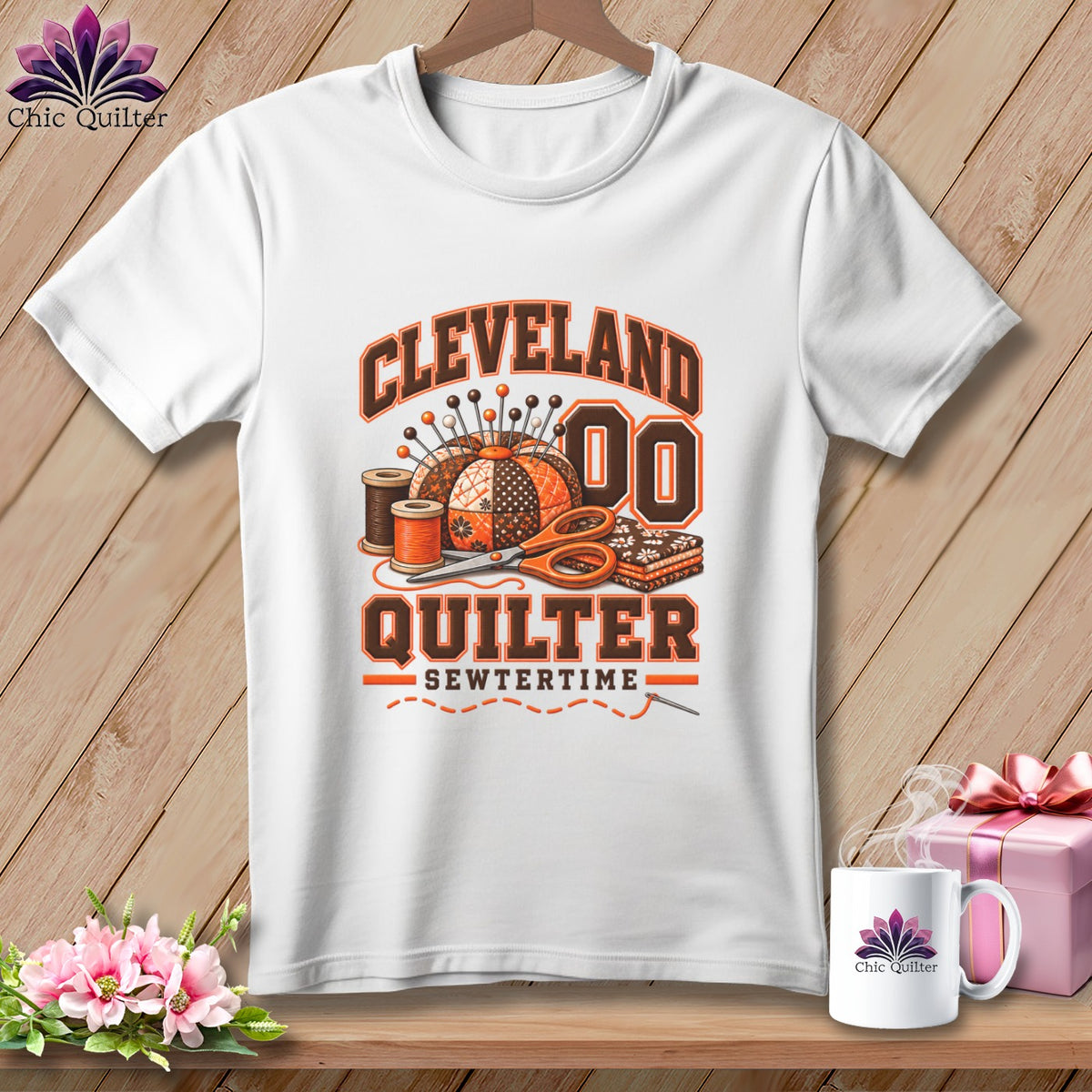 A white t-shirt features a Cleveland Quilter graphic with sewing tools and text on a wooden background.