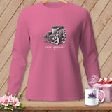 Pink long-sleeve shirt with a graphic of an armchair, quilt, and mug reading 