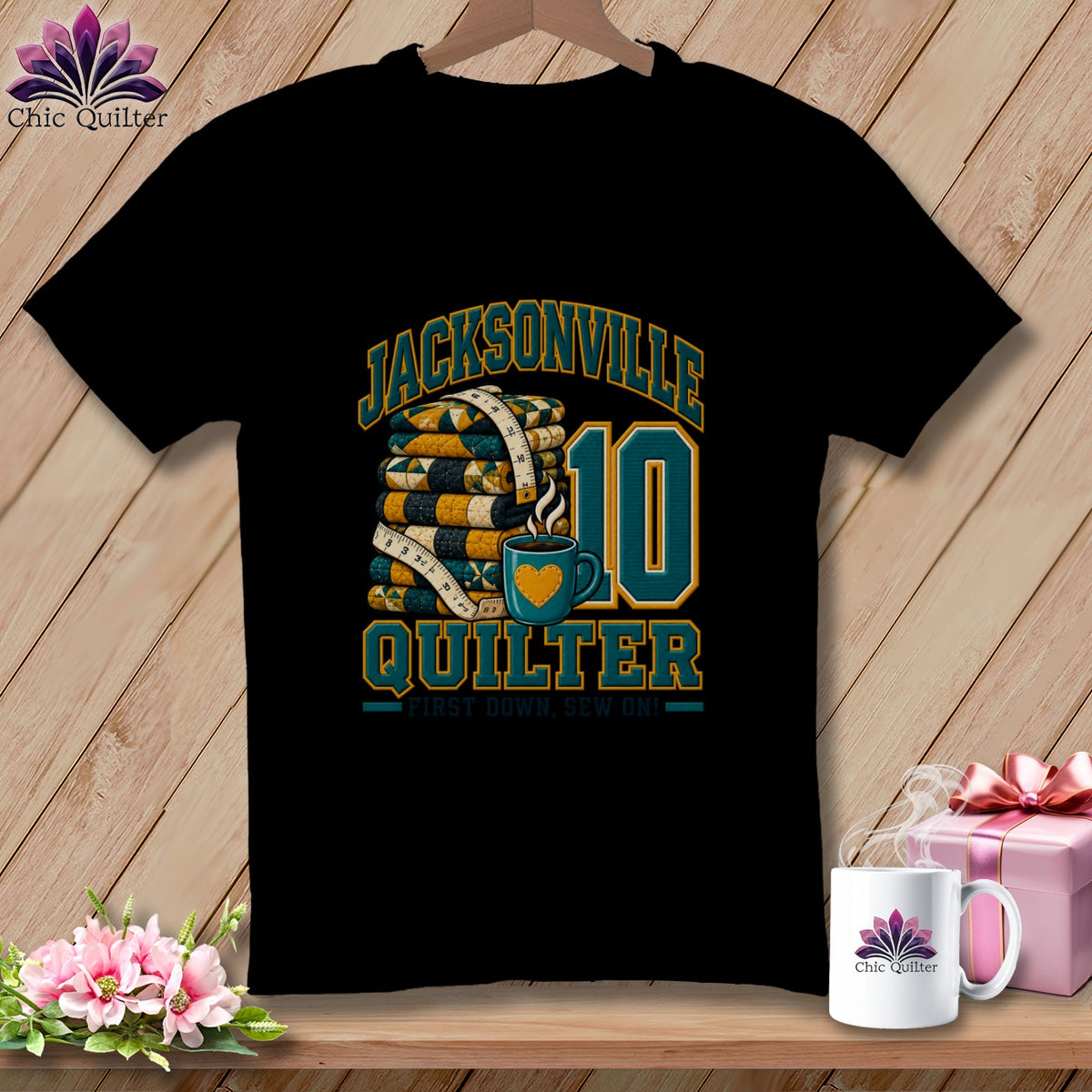 A black t-shirt featuring a graphic with Jacksonville Quilter text, a stack of quilts, a measuring tape, and a coffee mug.