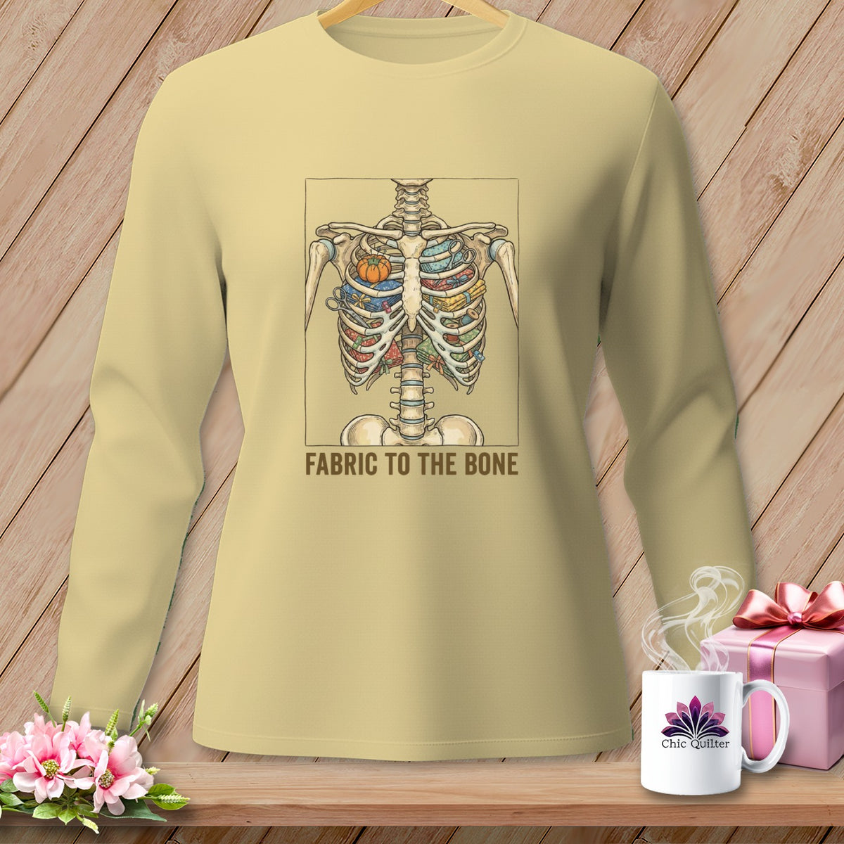 Light tan long-sleeve shirt with a skeleton graphic filled with colorful fabric scraps and the text "FABRIC TO THE BONE".