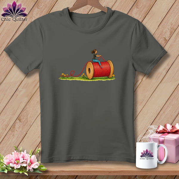 Charcoal gray crewneck t-shirt featuring a graphic of a woman riding a giant red spool of thread.