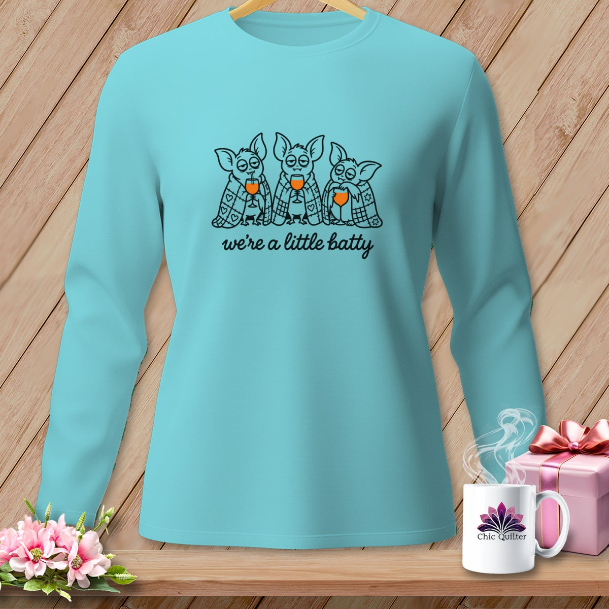 Teal long-sleeved shirt with three cartoon bats drinking and the text "we're a little batty".