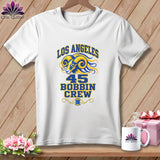 A white crewneck t-shirt with blue and yellow Los Angeles Bobbin Crew 45 graphic on a wooden background.