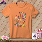 An orange short-sleeved t-shirt features a colorful graphic of four giraffes with quilts and sewing supplies.