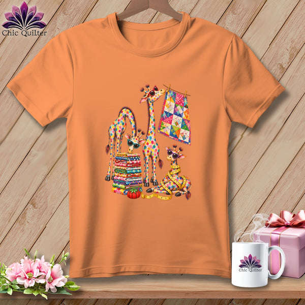 An orange short-sleeved t-shirt features a colorful graphic of four giraffes with quilts and sewing supplies.