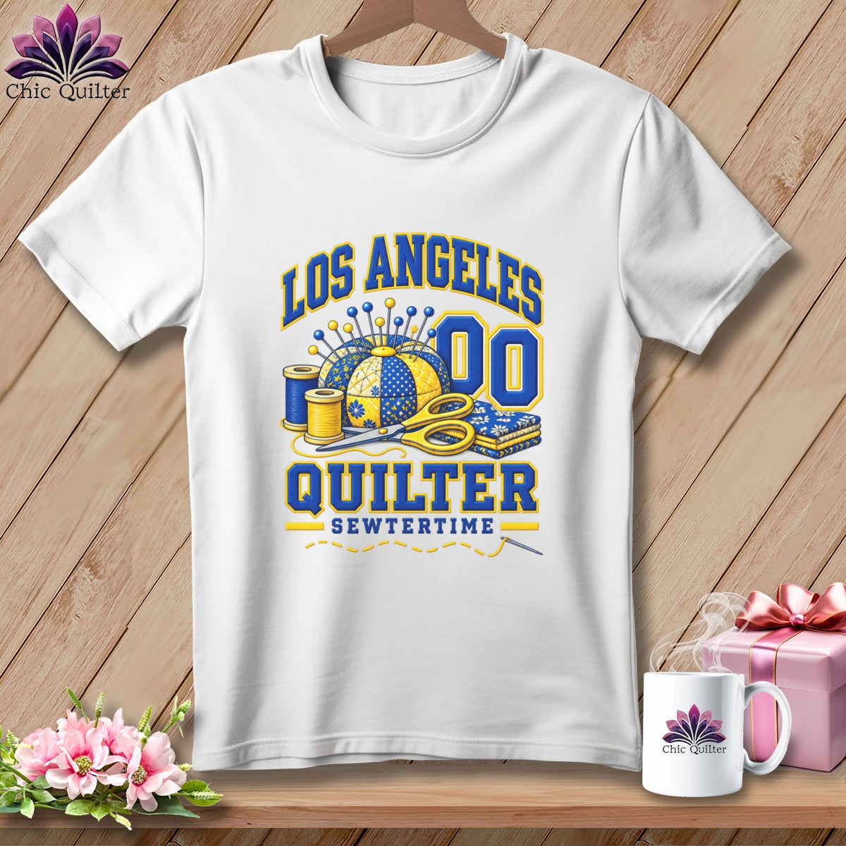 A white t-shirt featuring a blue and yellow Los Angeles Quilter graphic with sewing tools.