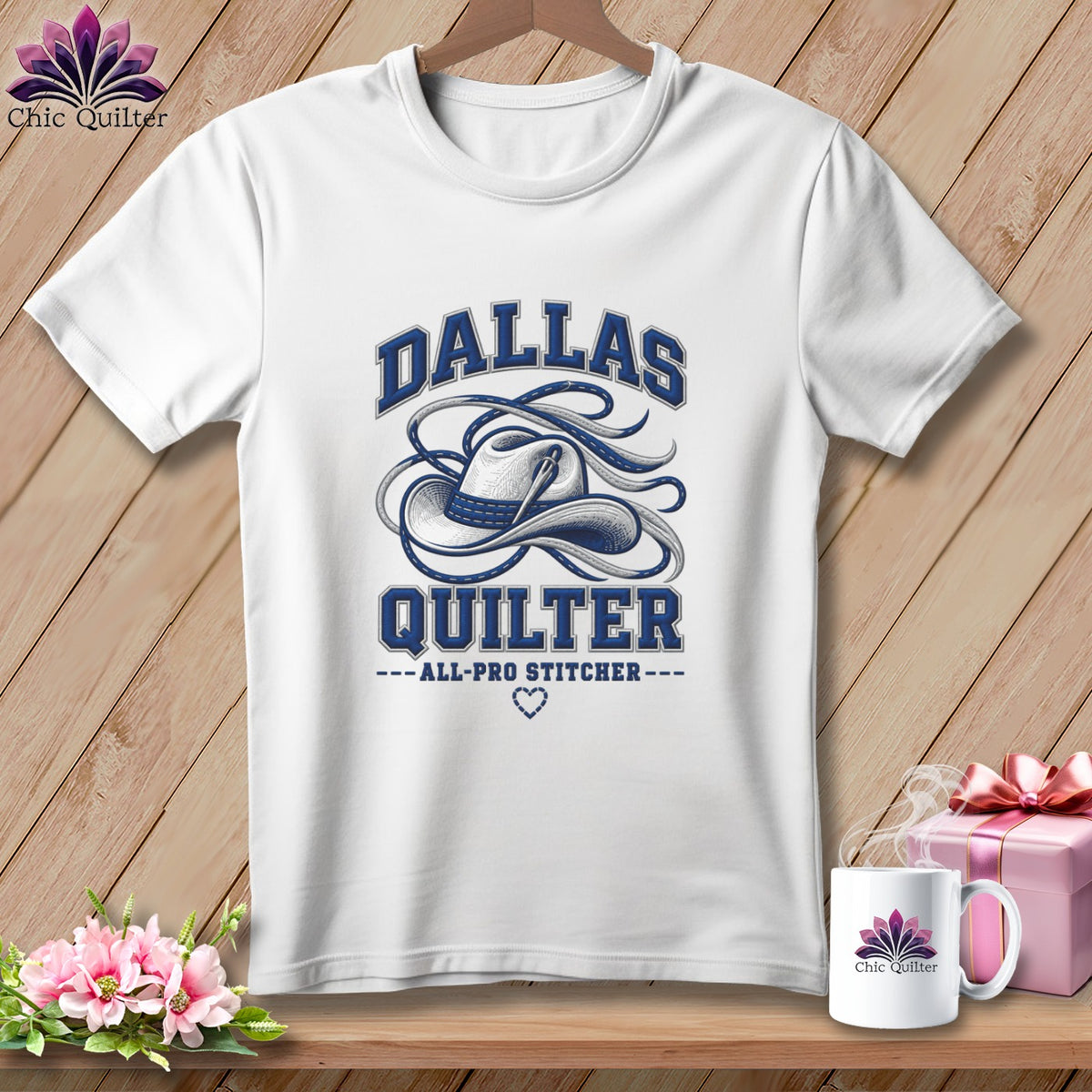 White t-shirt with blue Dallas Quilter cowboy hat graphic, hanging on a wooden background.