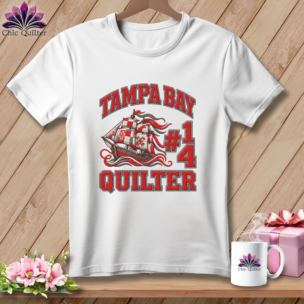 A white t-shirt featuring a Tampa Bay Quilter graphic with a pirate ship and patchwork sails.