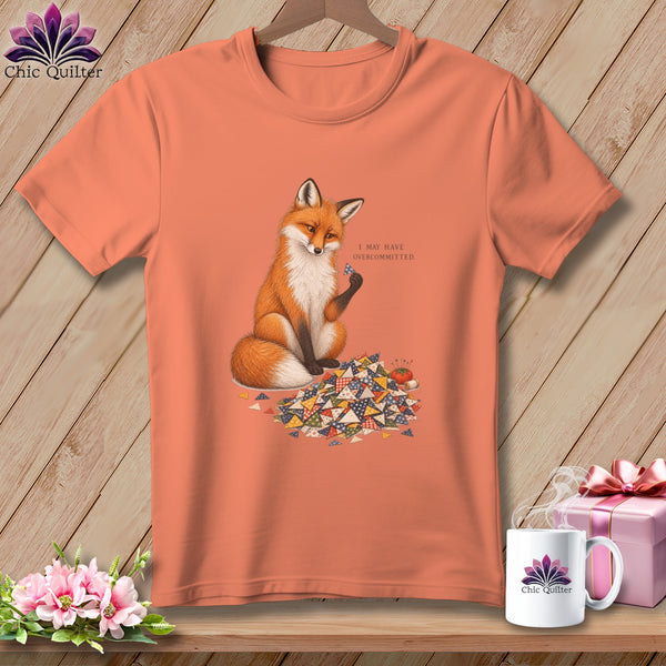 Peach t-shirt with a fox surrounded by quilt squares, holding a small fabric piece.