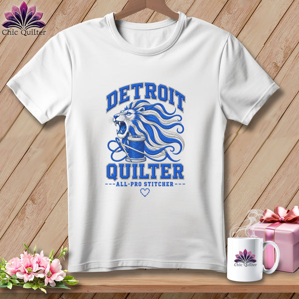 White t-shirt featuring a blue graphic of a roaring lion with a spool of thread and text reading Detroit Quilter.