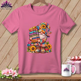 Pink t-shirt with a colorful gnome graphic holding a stack of fabric rolls, displayed on a wooden background.