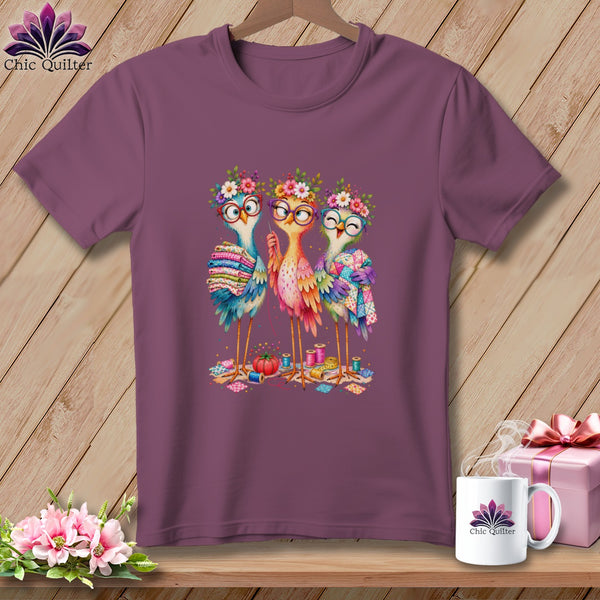 A plum t-shirt featuring a cartoon graphic of three colorful birds wearing glasses and flower crowns.