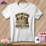 A white t-shirt features a graphic with the text New Orleans Quilter and rolls of fabric in a wooden crate.