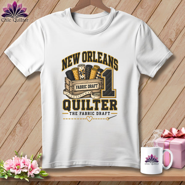 A white t-shirt features a graphic with the text New Orleans Quilter and rolls of fabric in a wooden crate.