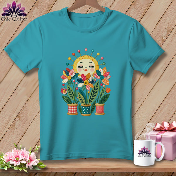 Teal t-shirt featuring a graphic of a smiling sun and colorful fabric flower pots on a wooden background.