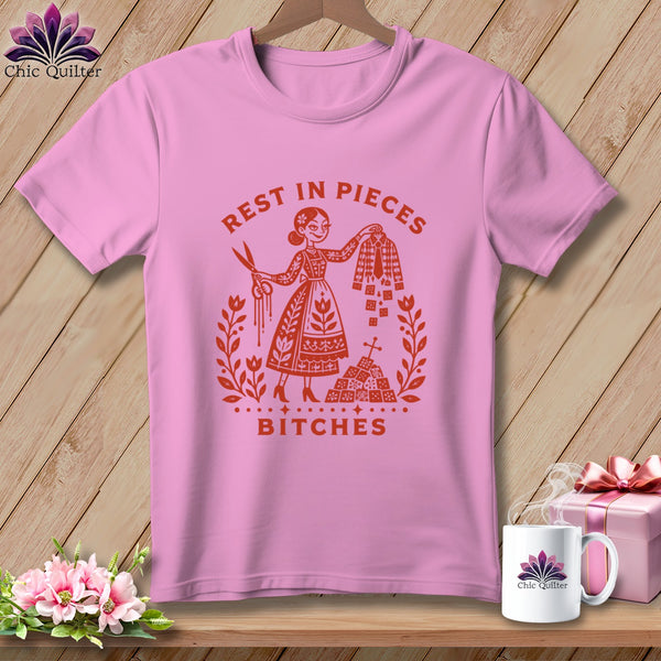 Pink t-shirt with "Rest in Pieces Bitches" text and graphic of woman with scissors and fabric.