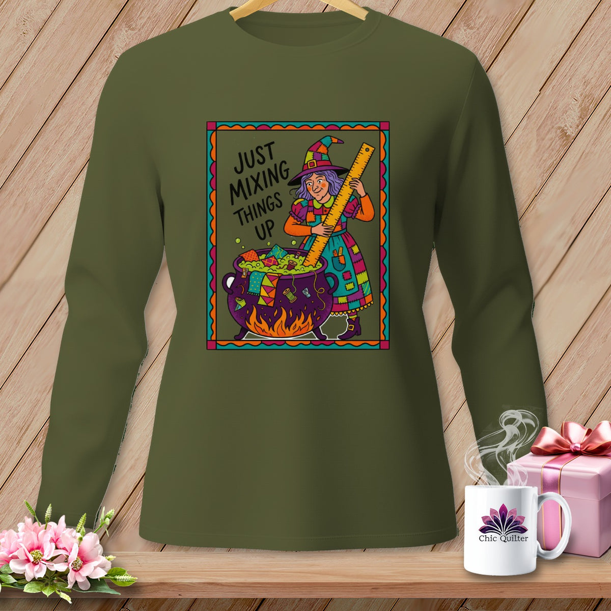 Green long-sleeve shirt with a graphic of a witch mixing in a cauldron. Text reads "Just Mixing Things Up".